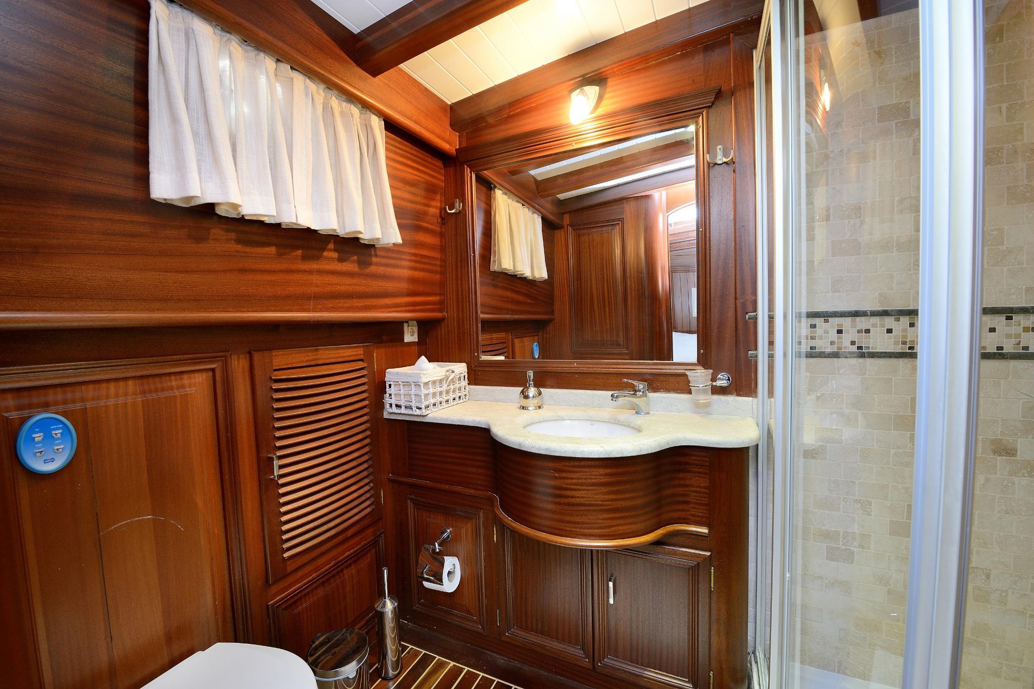 yacht bathroom featuring rich wood paneling, curved vanity with marble top and separate shower compartment