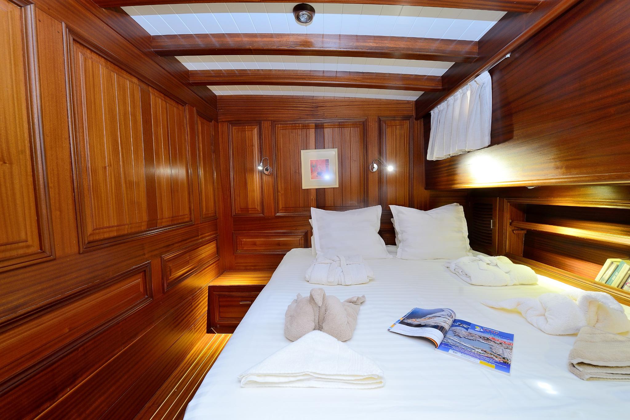yacht cabin interior with double bed, rich wood paneling, overhead skylight and reading lights