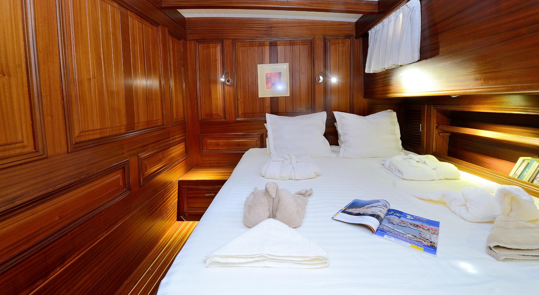 yacht guest cabin featuring double bed with white linens and rich teak wood paneling