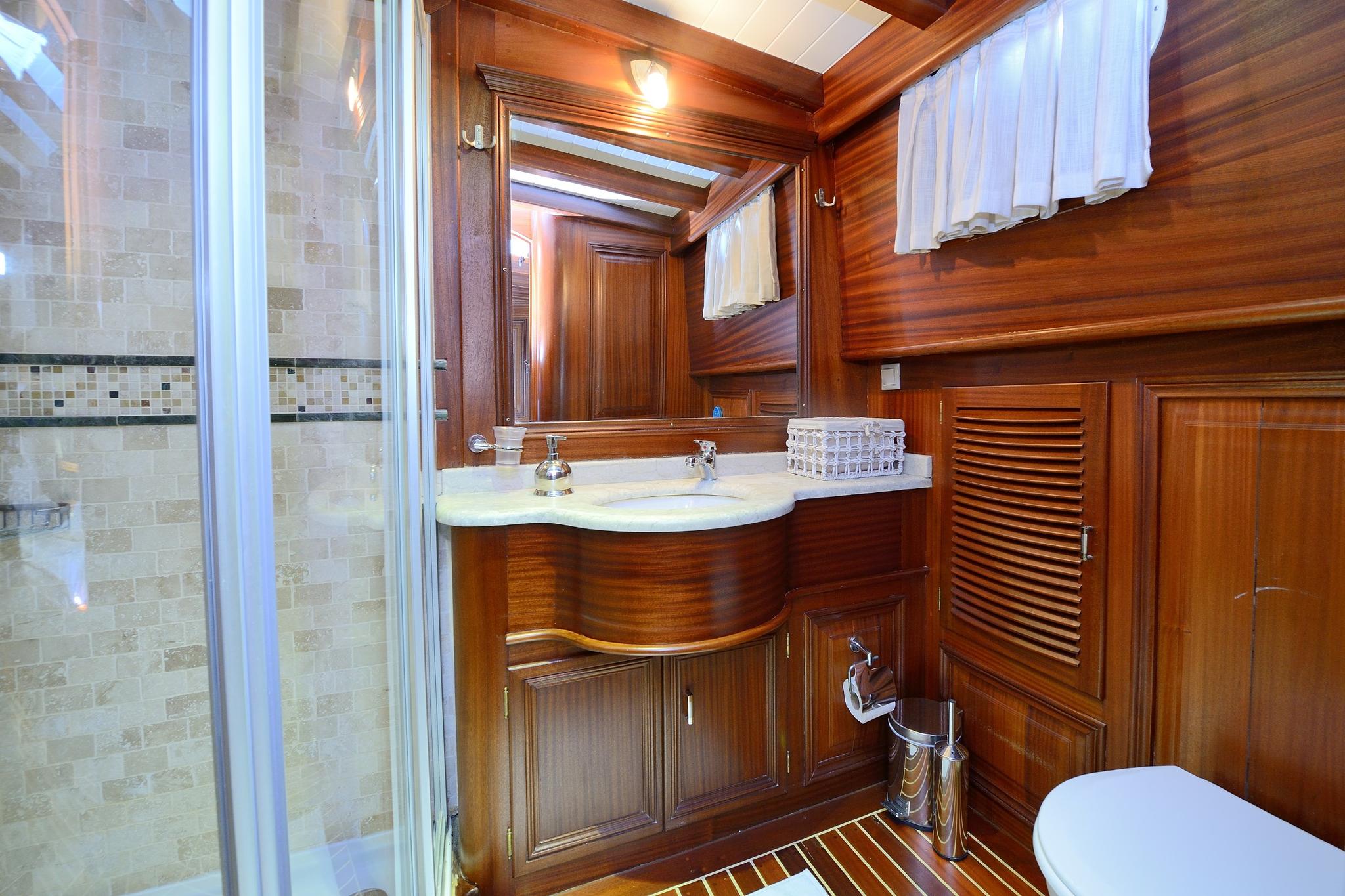 luxury yacht bathroom featuring curved wooden vanity, marble countertop, glass shower enclosure and teak finishes
