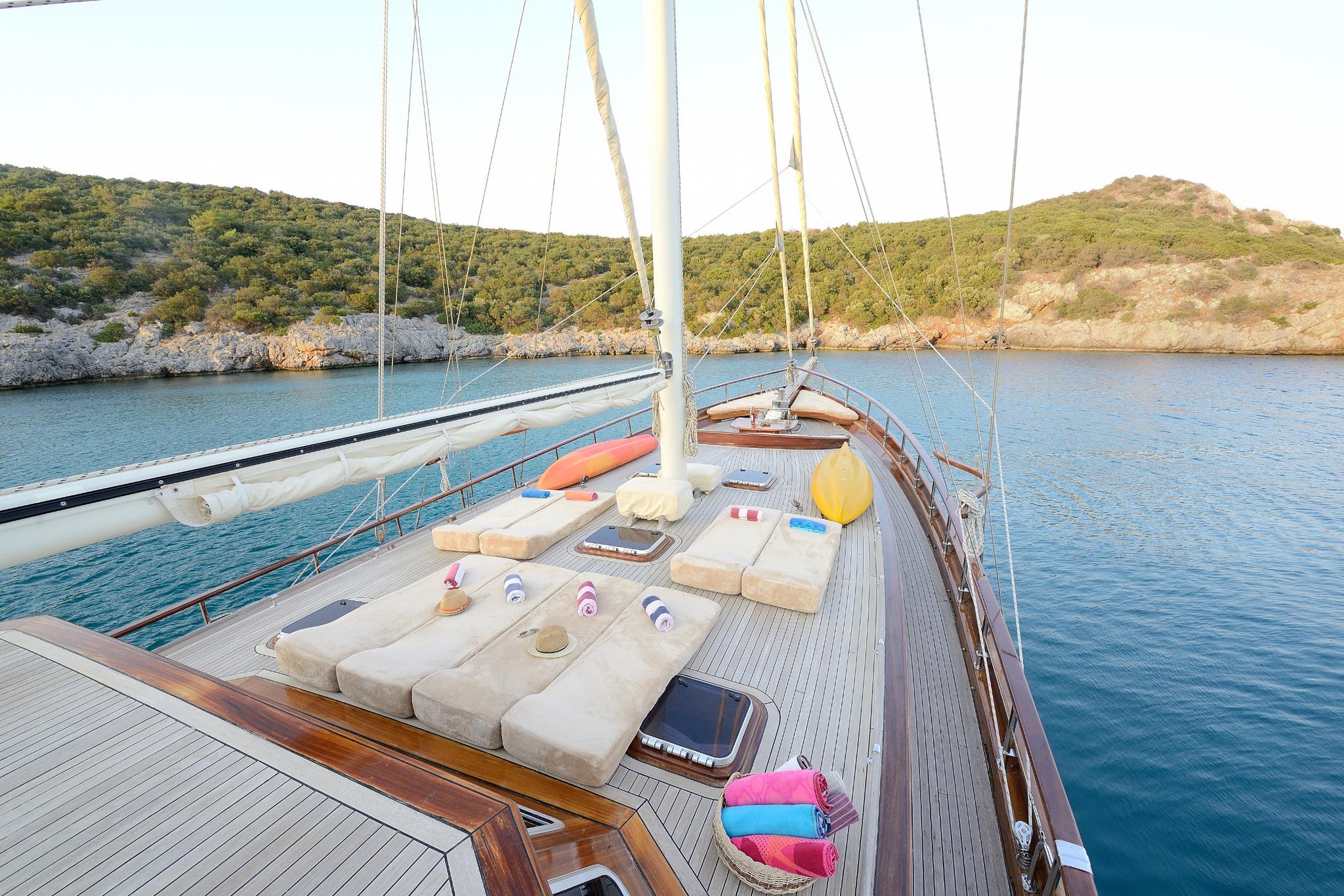 gulet bow deck with beige sun cushions, water toys, and teak decking in secluded bay