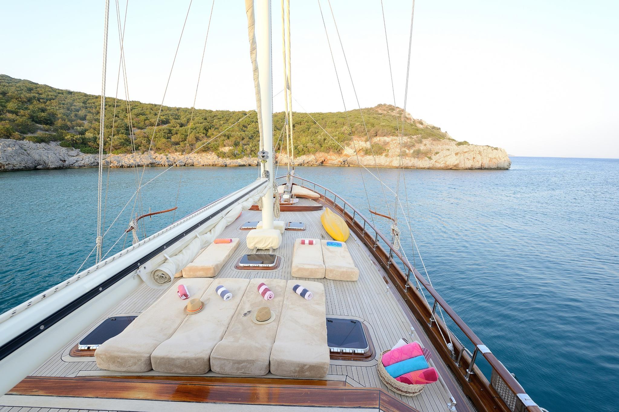 gulet bow deck with beige sunbathing cushions, mast, and rigging anchored in Mediterranean bay
