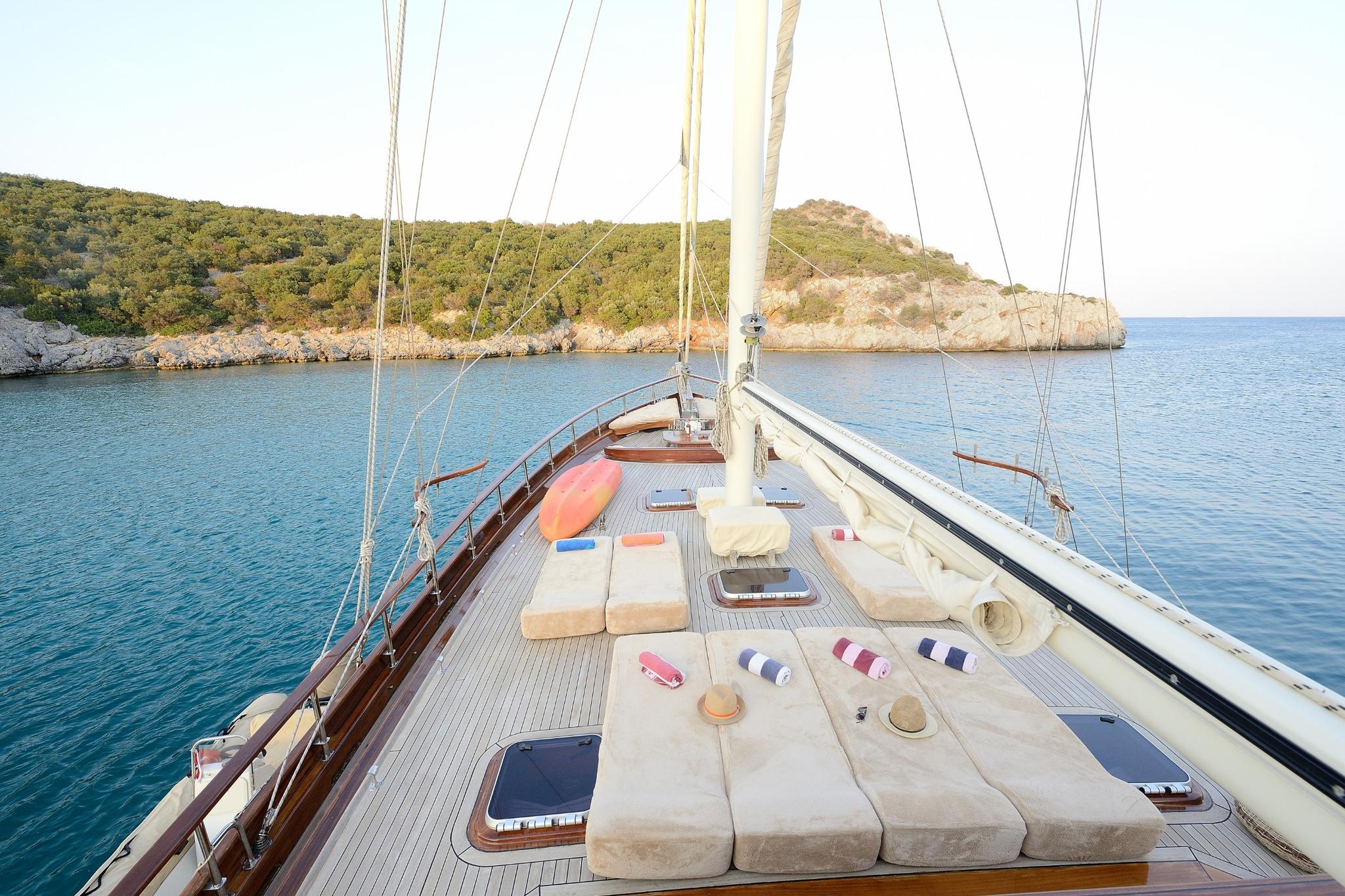 gulet bow deck with cream sunbathing cushions, white mast, and teak decking anchored in Mediterranean bay