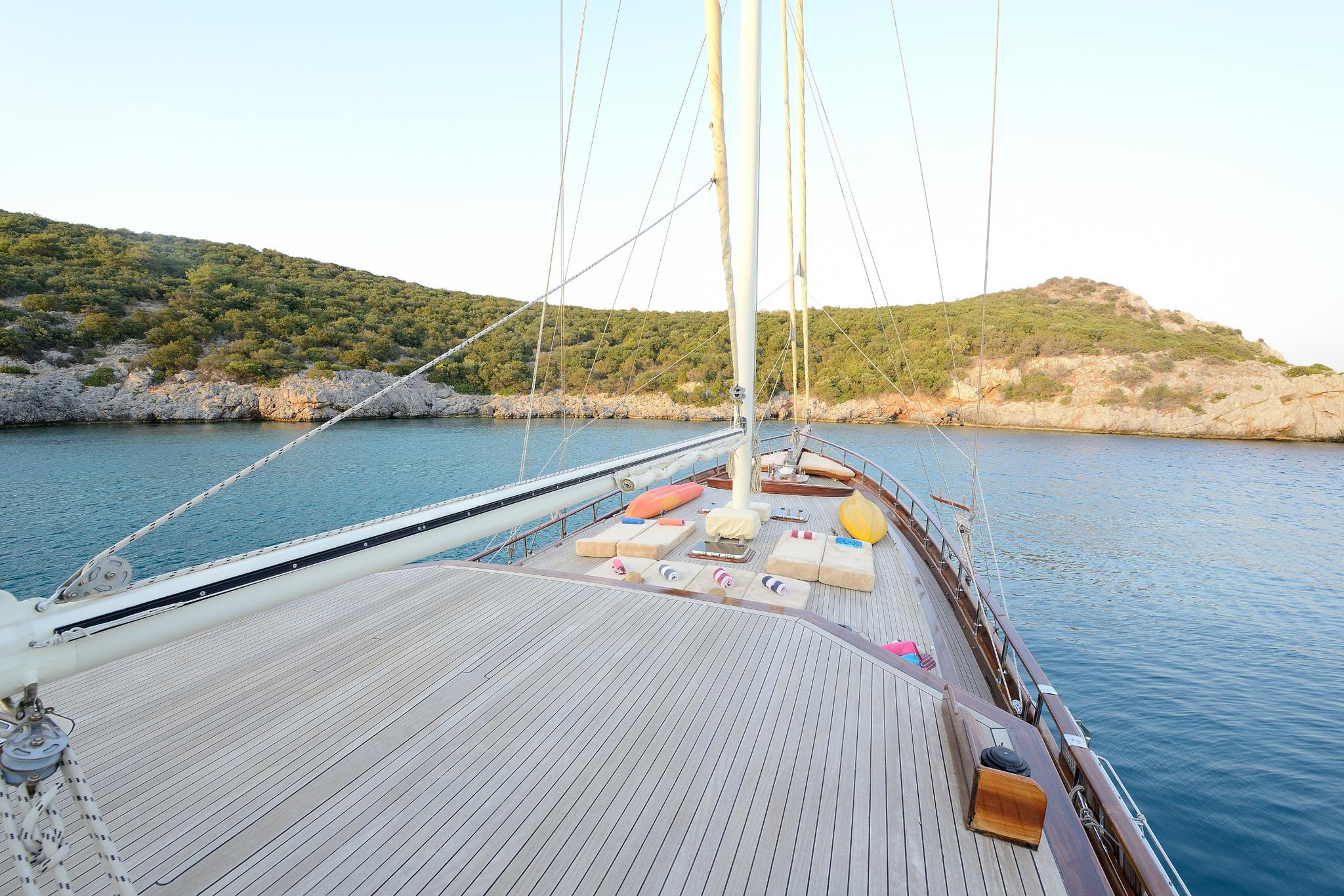 gulet bow deck with teak planking, cushioned sunbathing area, and white mast at anchor
