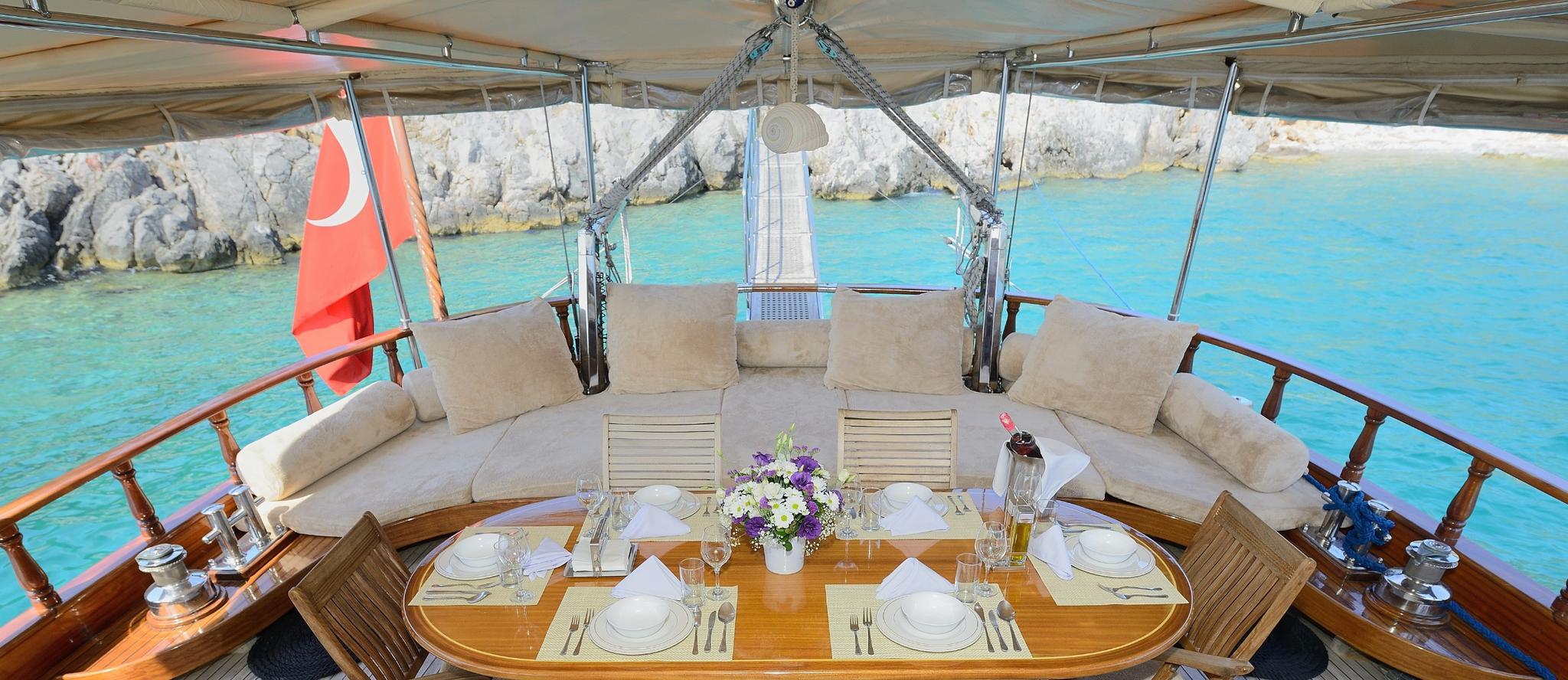 gulet aft deck dining area with oval teak table, place settings, and cushioned seating overlooking turquoise waters