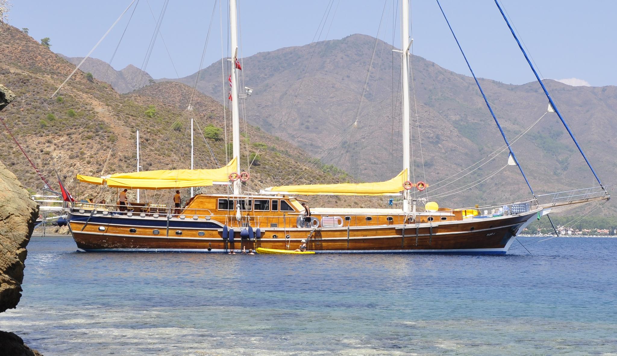 Traditional wooden gulet with yellow awnings anchored in calm bay with rocky mountains