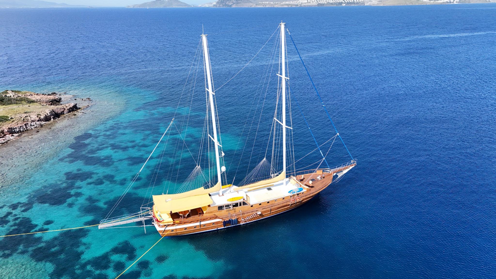 aerial view of traditional wooden gulet with two masts anchored in crystal clear turquoise bay