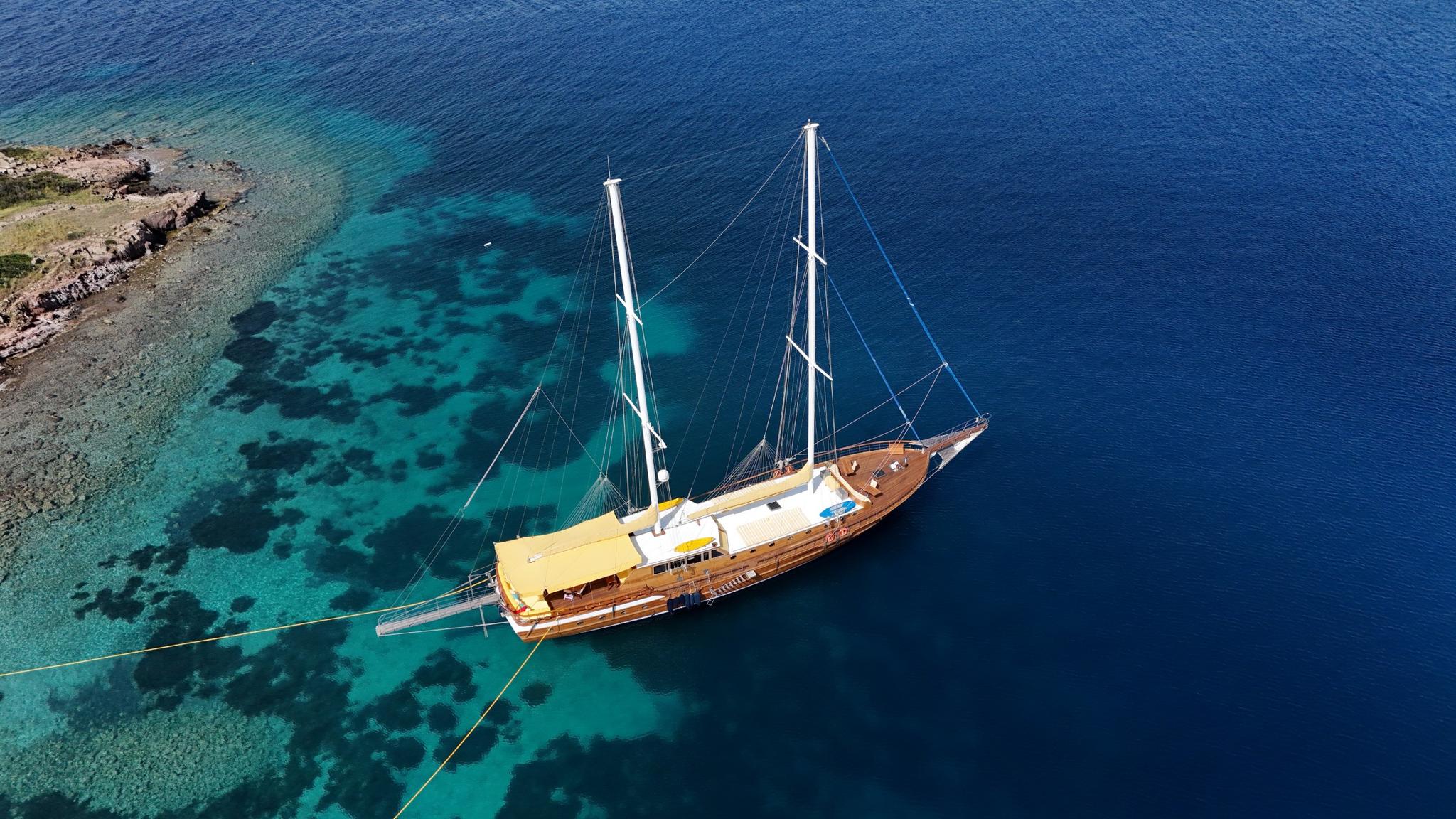 aerial view of traditional wooden gulet yacht anchored near rocky coastline in crystal clear Mediterranean waters