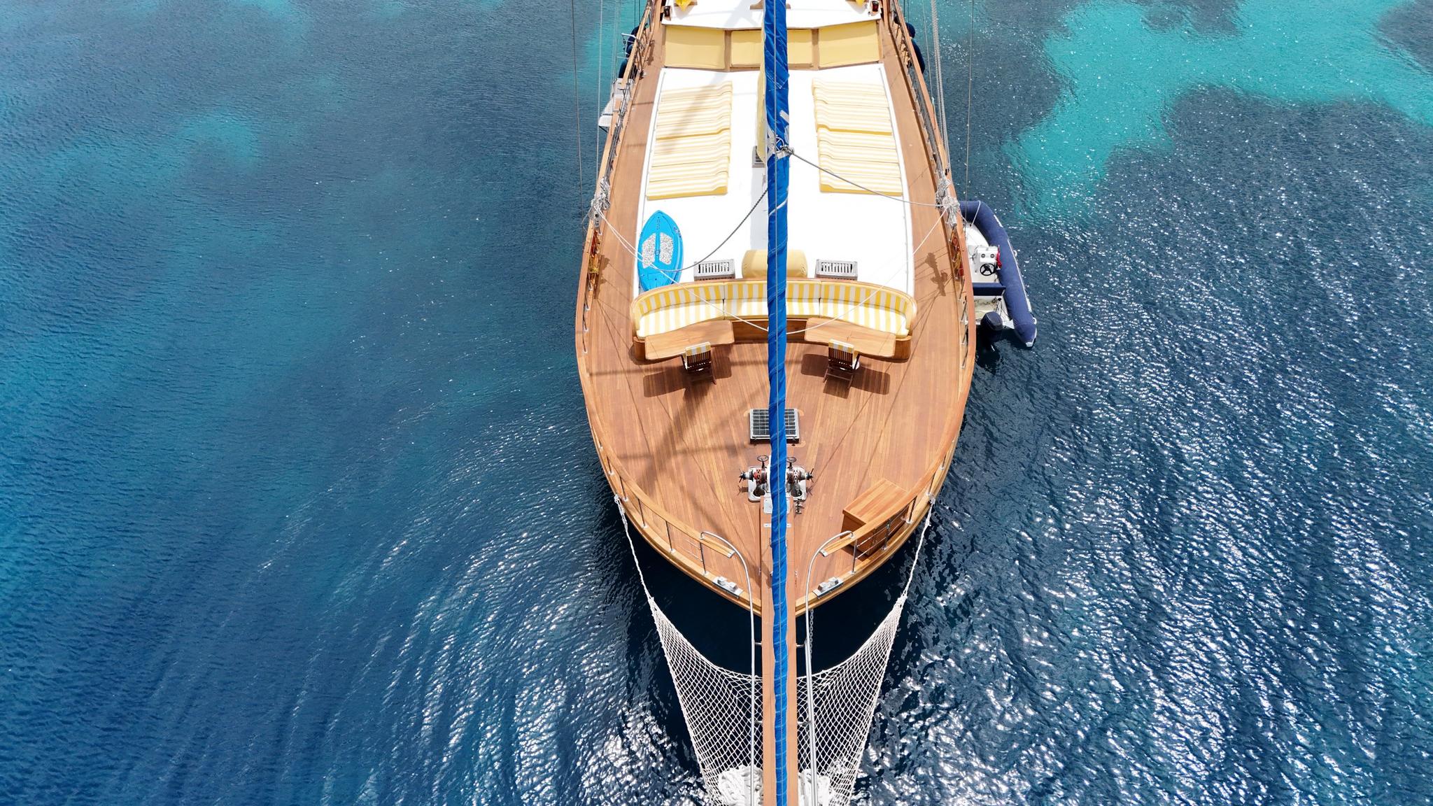 aerial view of traditional wooden gulet with blue mast and teak decking anchored in turquoise waters