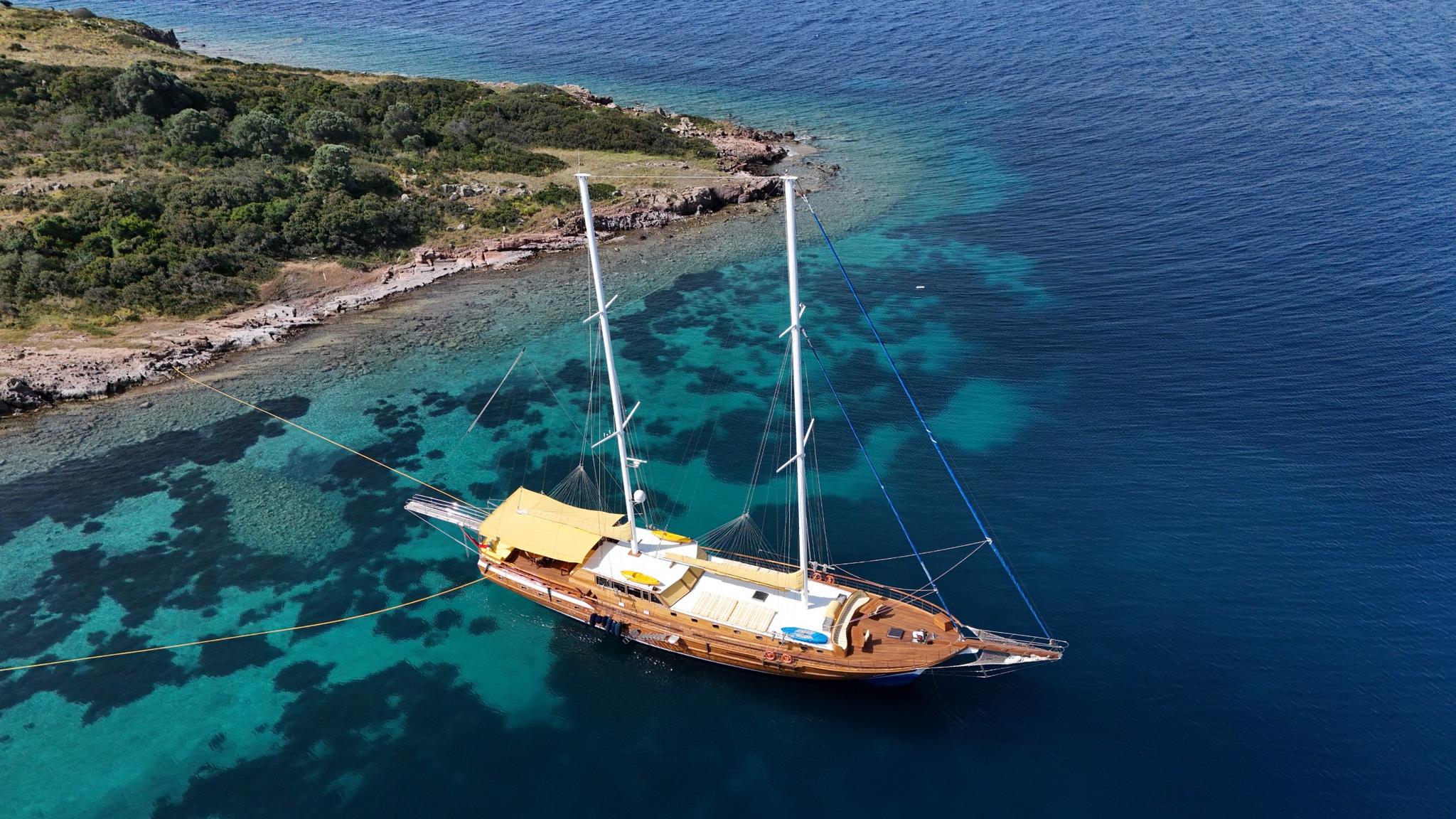 aerial view of wooden gulet yacht anchored in crystal clear turquoise waters near Mediterranean coastline