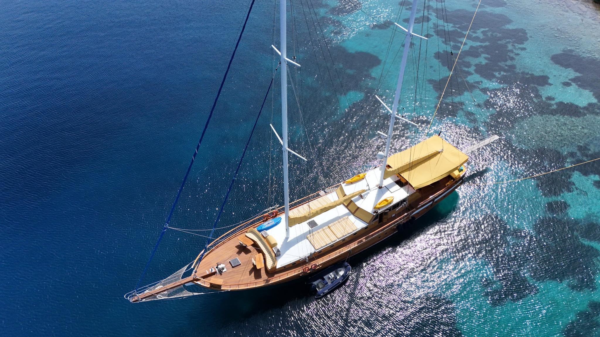 aerial view of traditional wooden gulet with two masts anchored in crystal clear turquoise bay