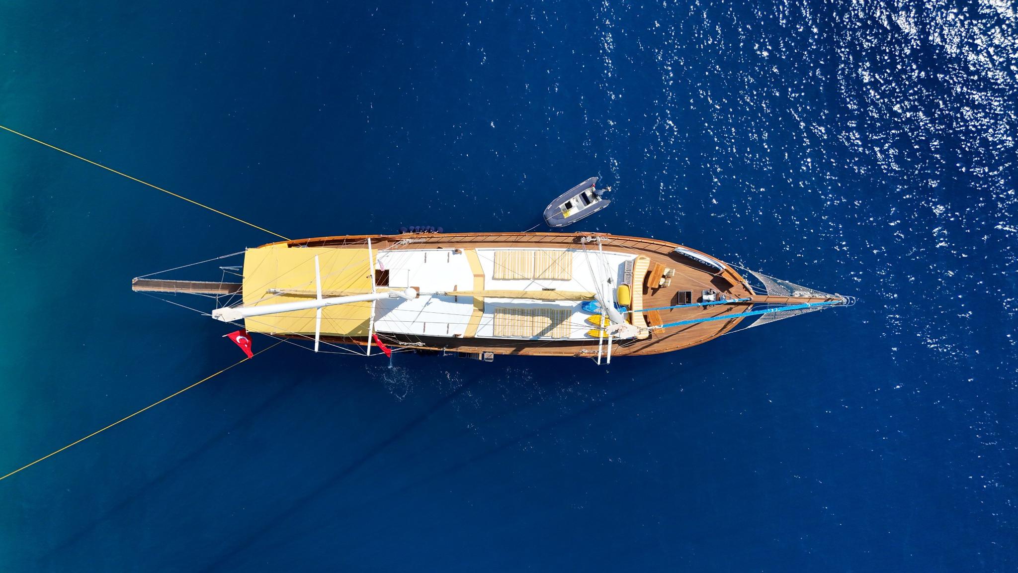 aerial view of wooden gulet yacht with tender boat anchored in crystal blue waters