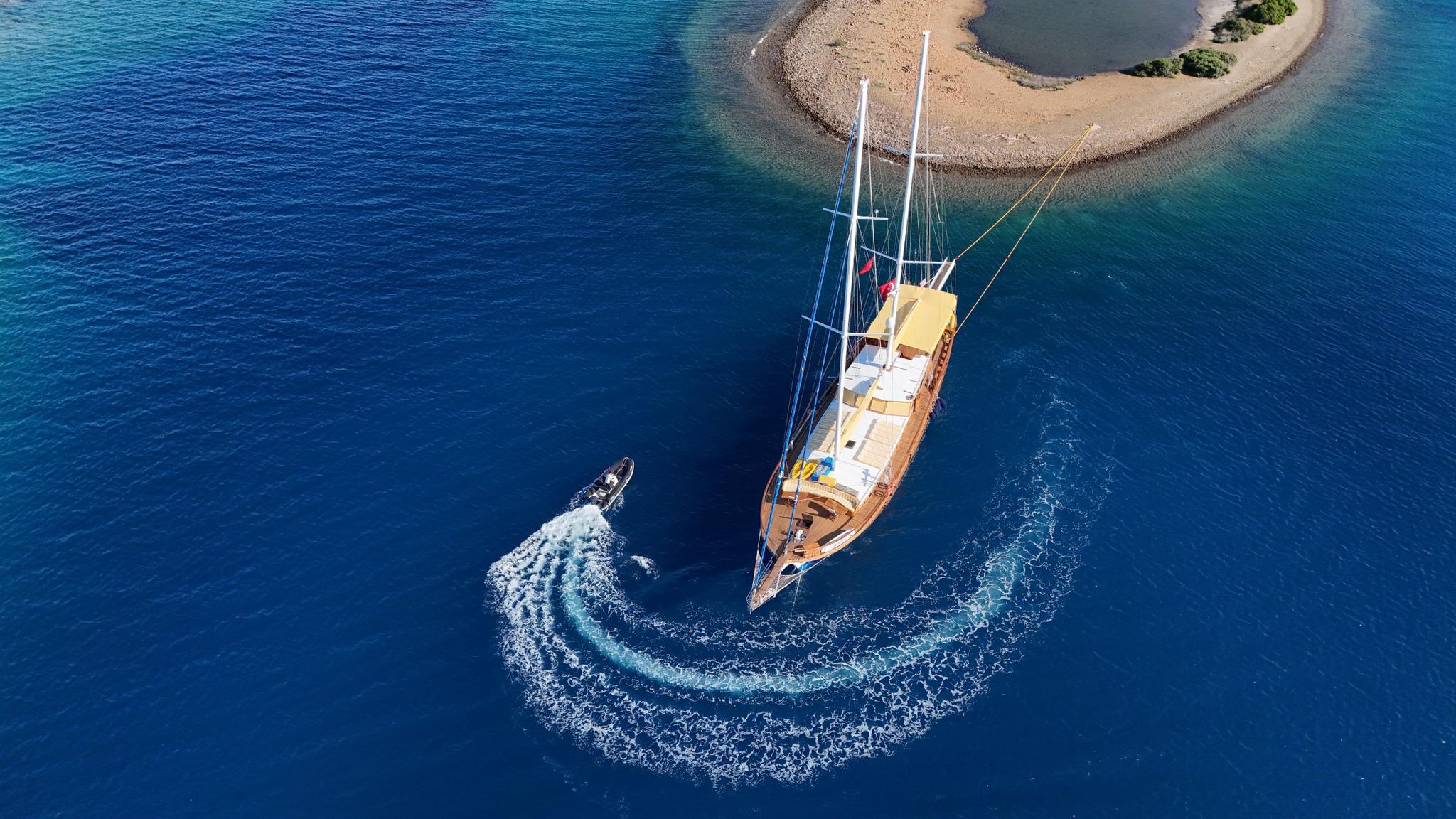 aerial view of traditional gulet yacht anchored in turquoise waters with tender boat creating circular wake