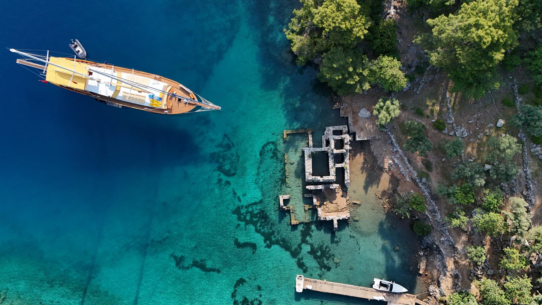aerial view of luxury gulet yacht anchored in crystal clear turquoise waters near ancient stone ruins