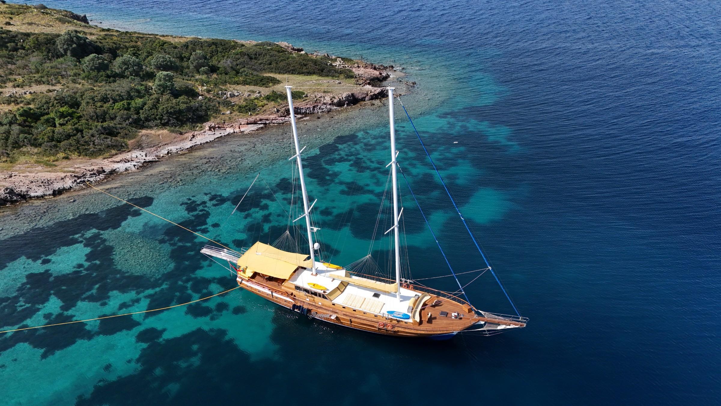 aerial view of wooden gulet yacht anchored in crystal clear turquoise waters near Mediterranean coastline