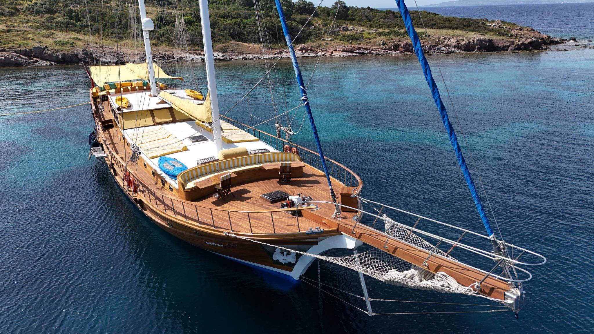 Aerial view of wooden gulet with teak decks anchored in crystal clear turquoise waters near rocky coastline