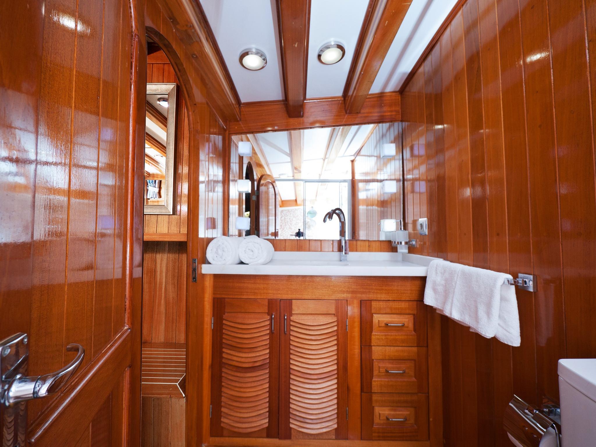 yacht bathroom featuring polished wood vanity, white basin, mirror and towels