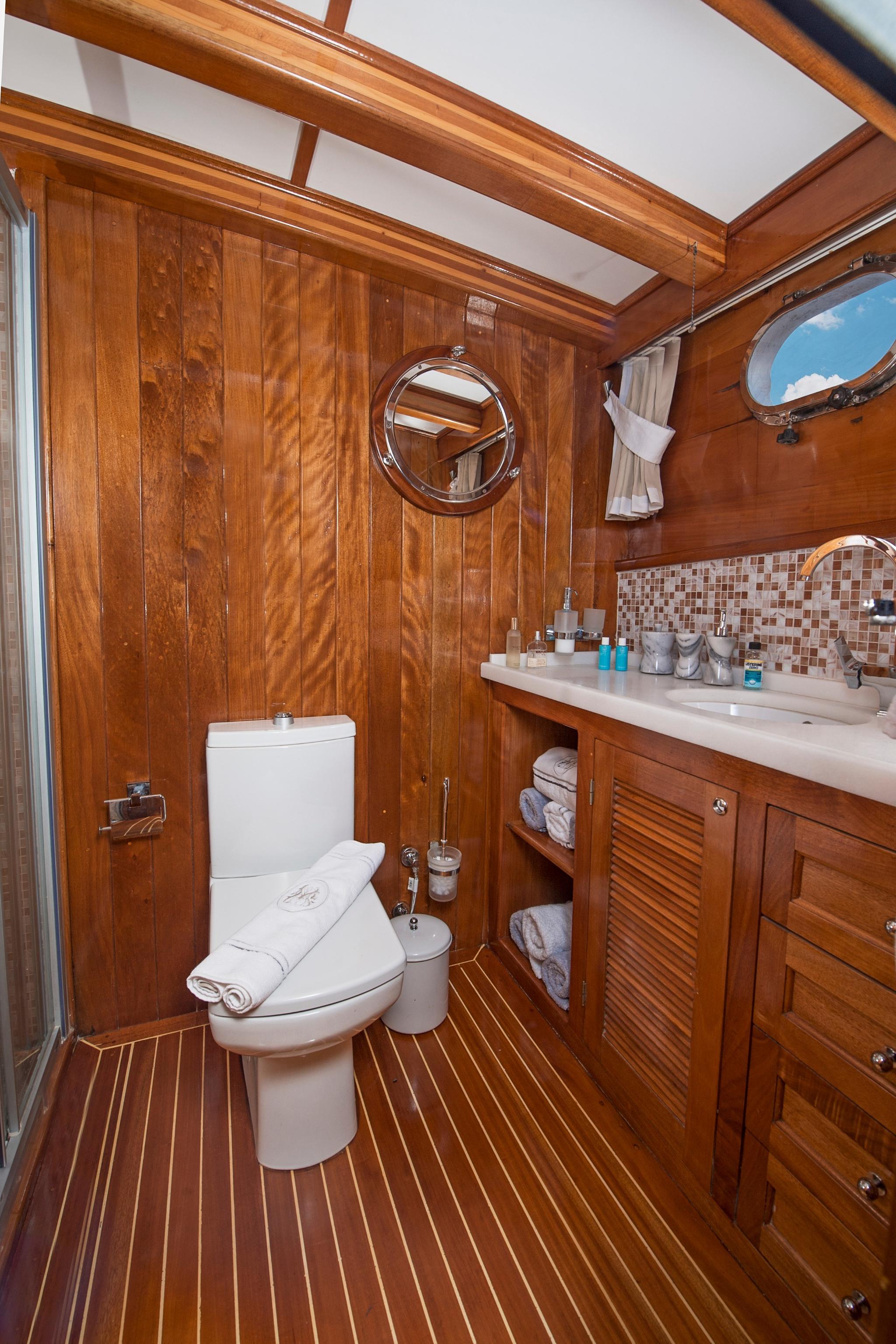 yacht bathroom featuring white toilet, marble vanity counter, teak wood paneling and mosaic backsplash