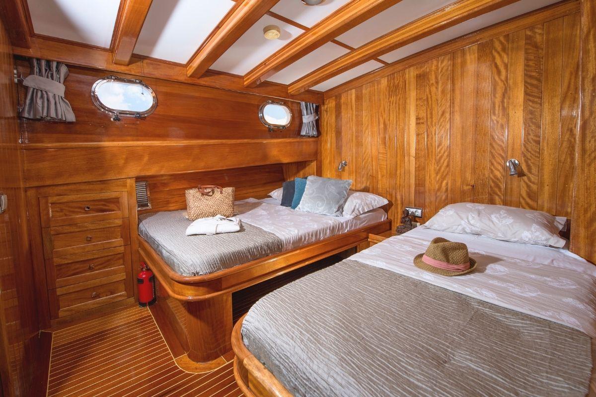 Twin guest cabin with two single beds, wooden paneling, portholes and built-in storage