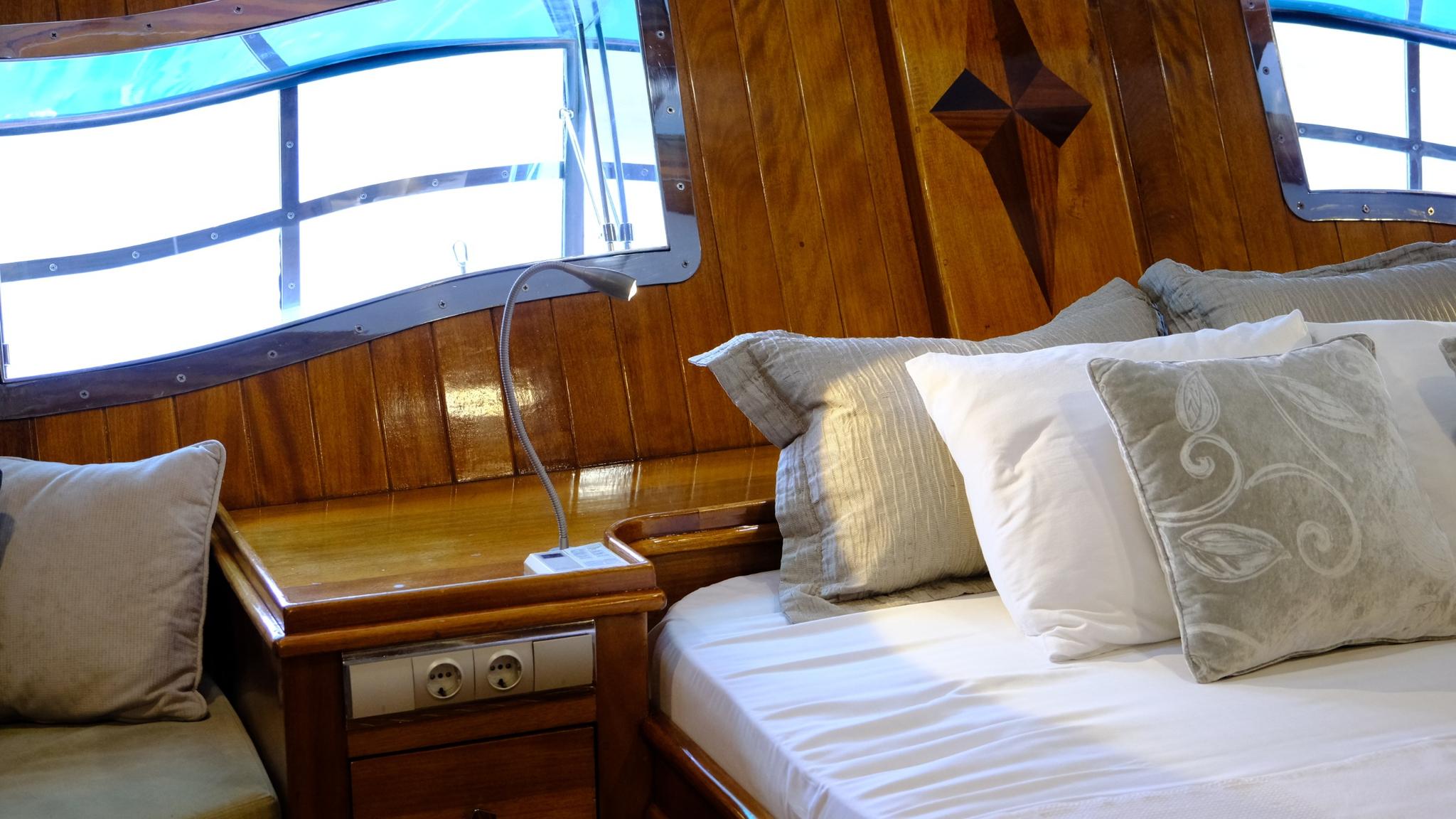 yacht guest cabin with white bedding, decorative pillows and brass porthole windows