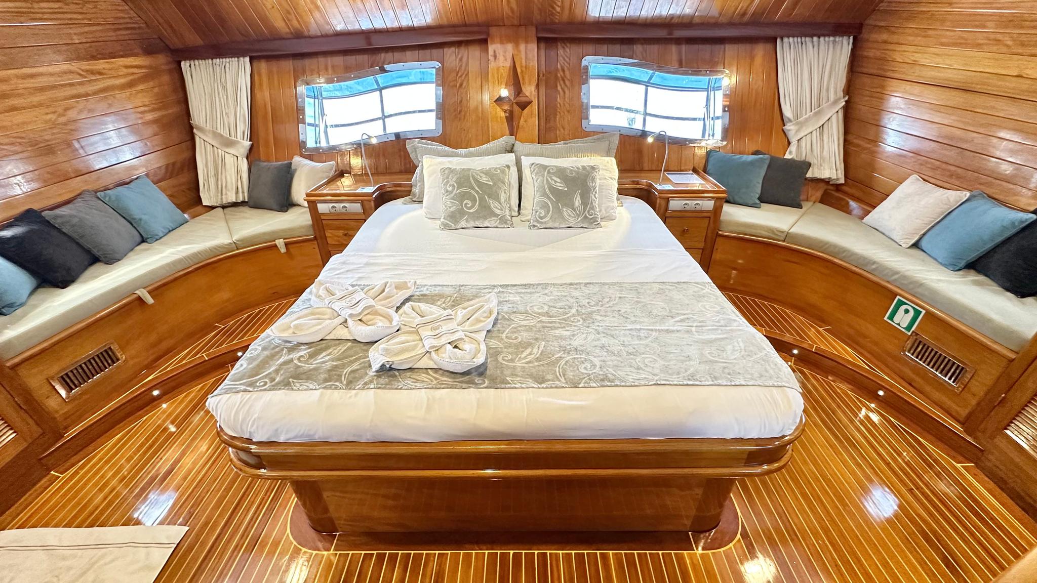 luxury yacht master cabin featuring king bed, built-in seating benches, wooden paneling and dual portholes