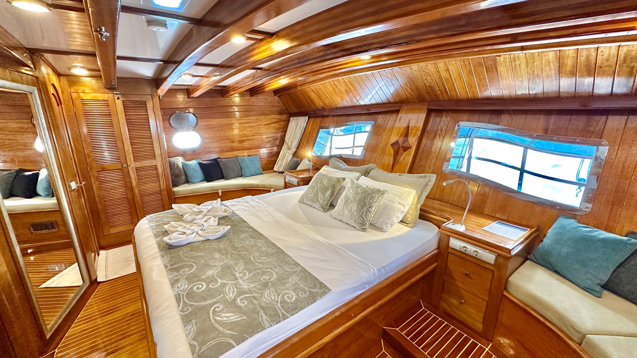 master cabin interior with king bed, built-in seating, wooden paneling and portholes
