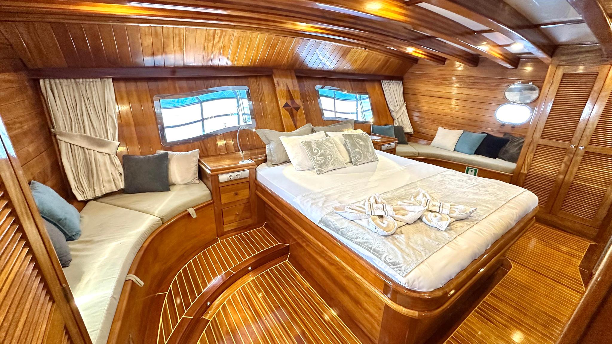 luxury yacht master cabin with double bed, built-in seating, portholes and wooden interior