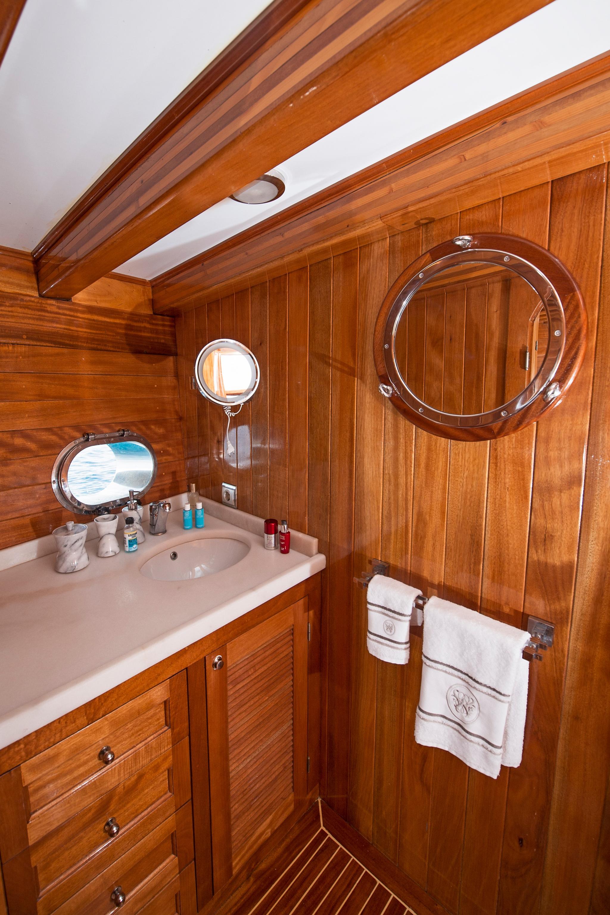 yacht bathroom with white sink, circular porthole window, wooden cabinetry and towel rack
