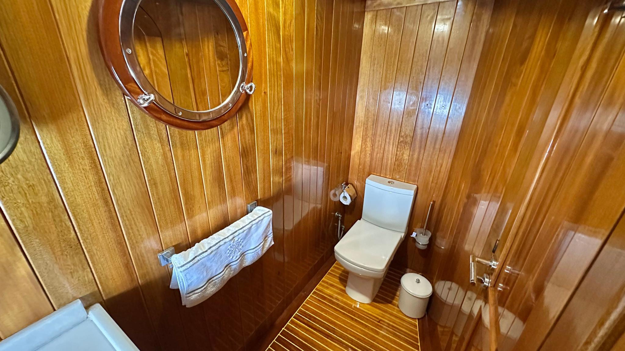 yacht bathroom interior with white toilet, wooden wall paneling and porthole window