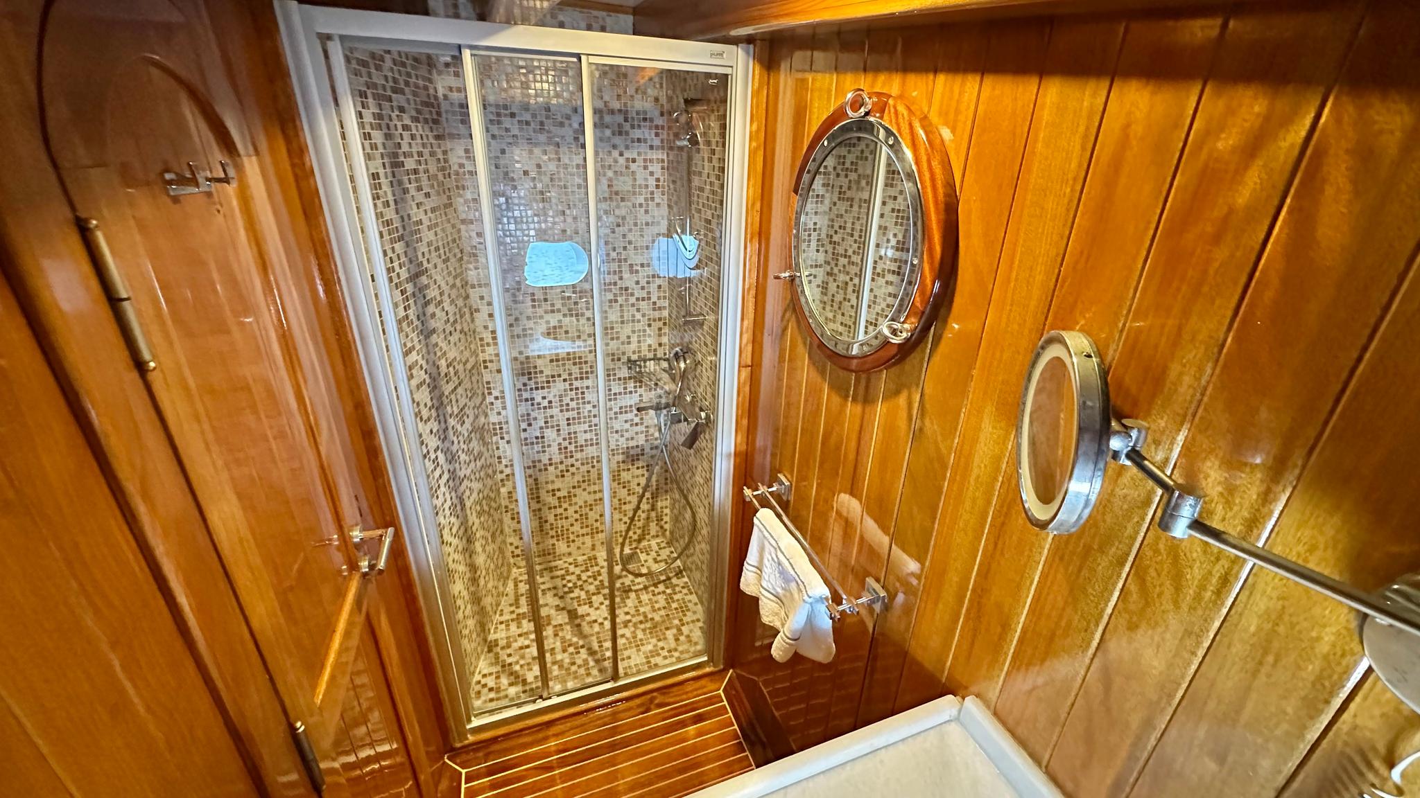 yacht bathroom featuring tiled shower stall with glass doors and nautical porthole mirror