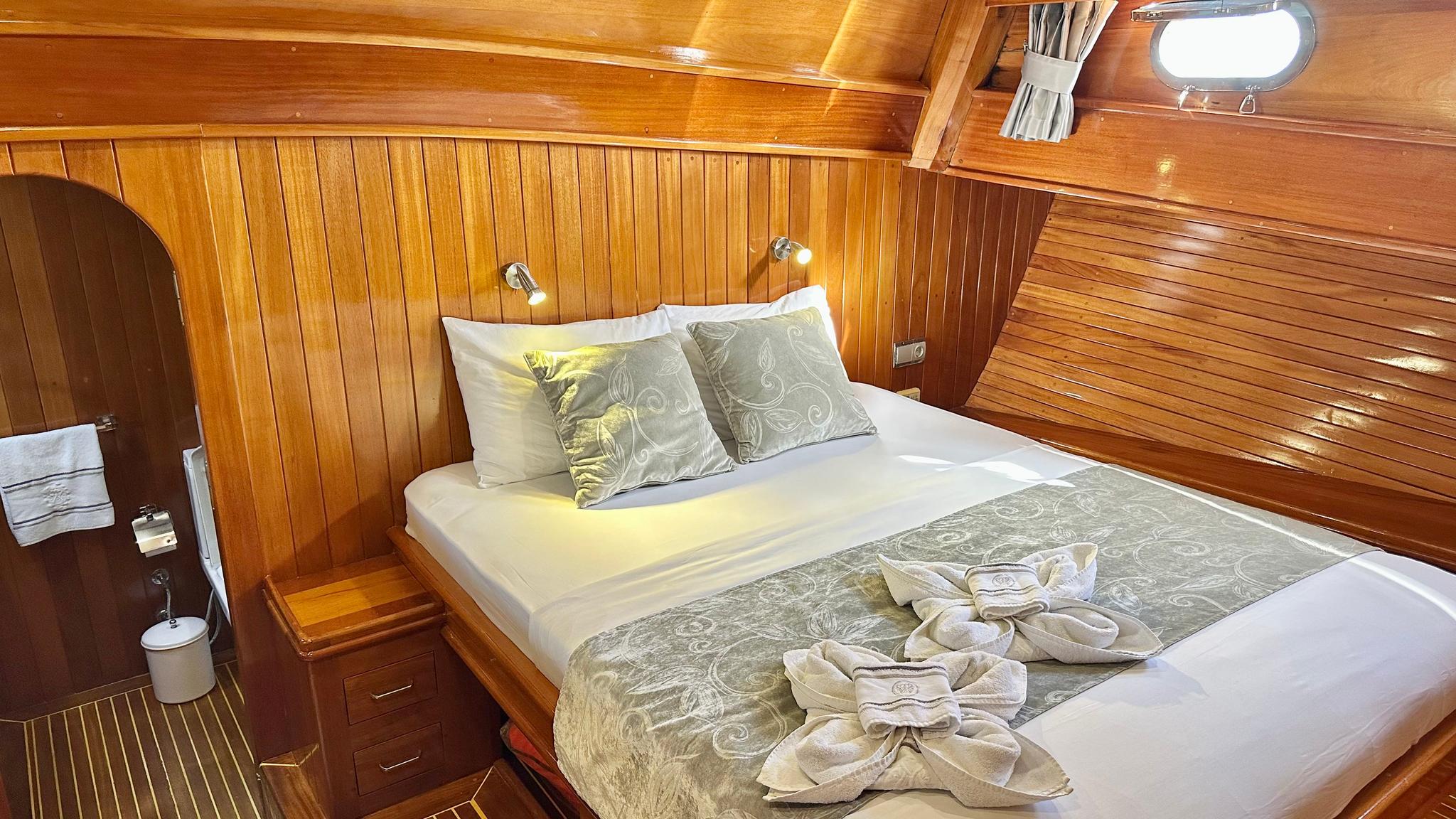 yacht guest cabin with double bed, wooden paneling, reading lights and porthole window