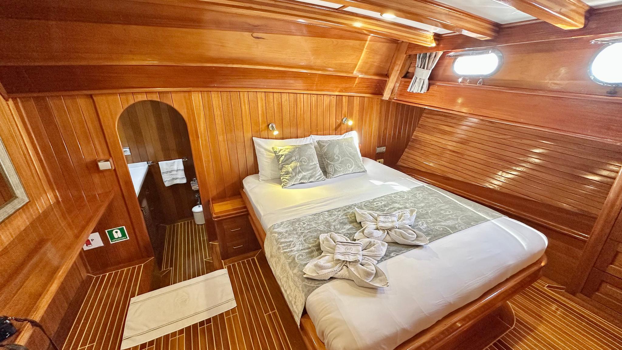 yacht guest cabin with double bed, wooden paneling, portholes and towel arrangement