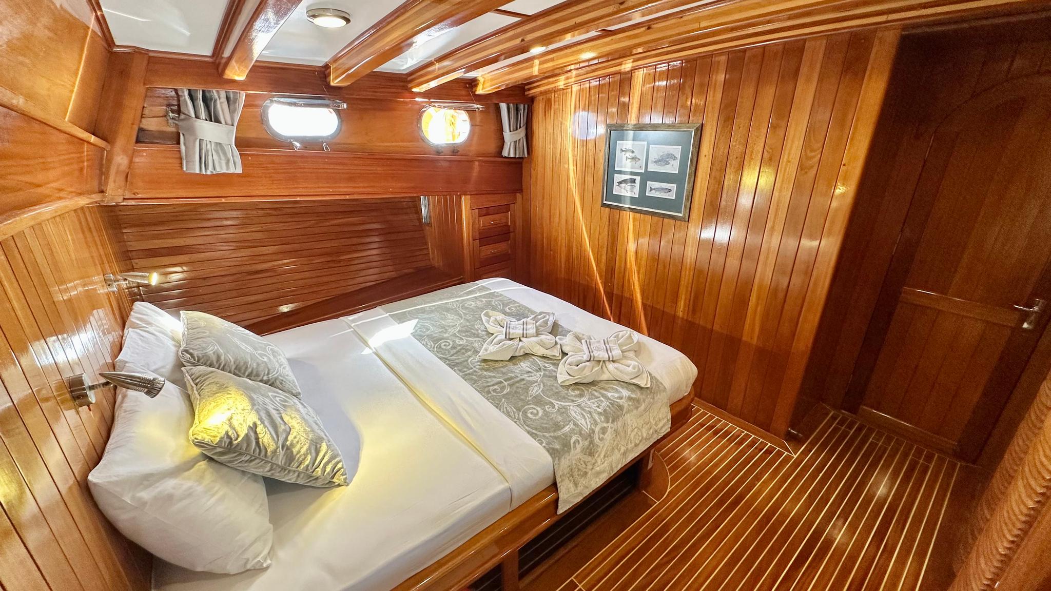 guest cabin interior with double bed, wooden walls, portholes and decorative towel swans