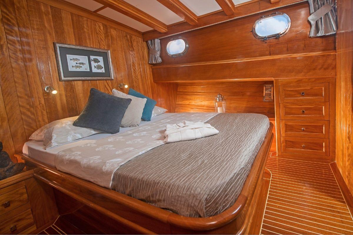 yacht guest cabin with double bed, wooden paneling, portholes and built-in storage