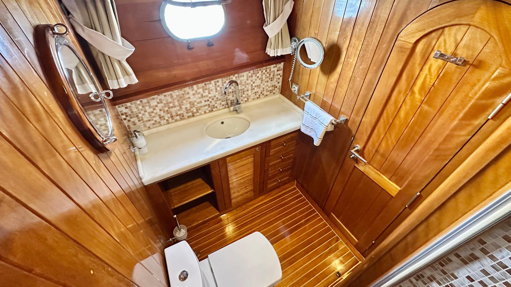 compact yacht bathroom featuring marble vanity, mosaic tile backsplash, porthole window and teak flooring