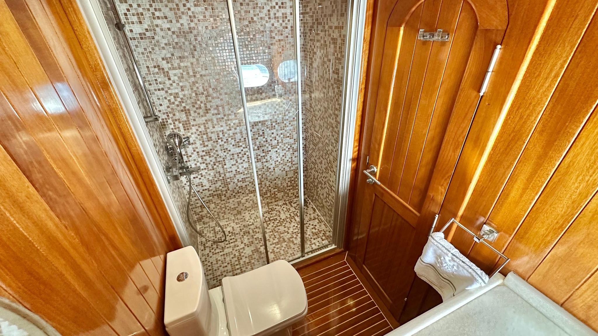 yacht bathroom interior with glass shower enclosure, mosaic tiles, and teak paneling