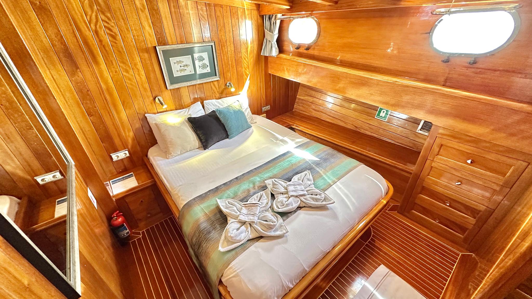 yacht guest cabin with double bed, wooden paneling, portholes and decorative towel arrangement