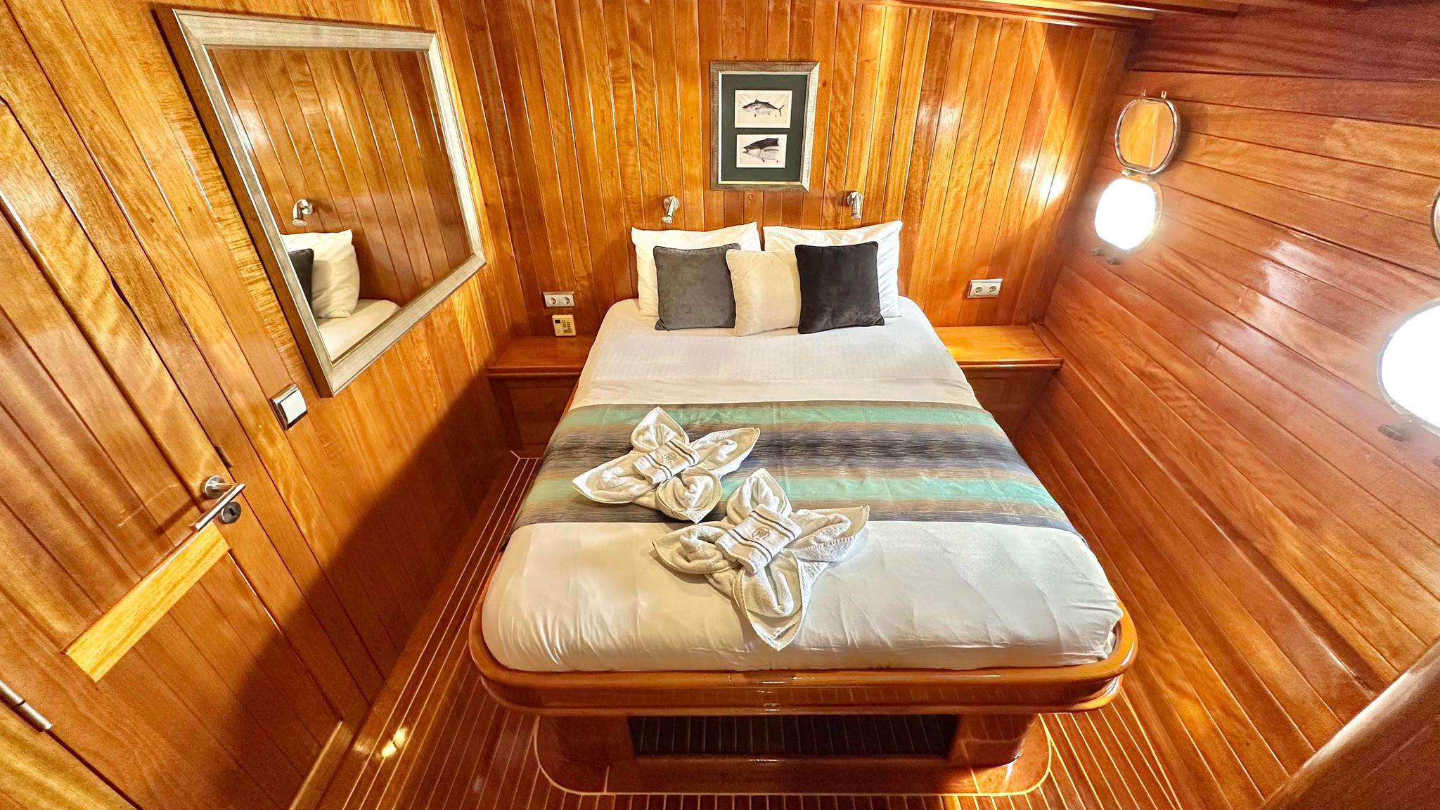 yacht guest cabin featuring double bed with striped runner, wooden wall paneling, mirror, and nautical artwork