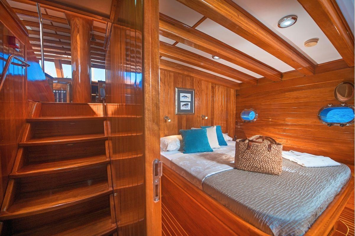 yacht guest cabin featuring double bed with blue pillows, wooden storage shelves, and portholes