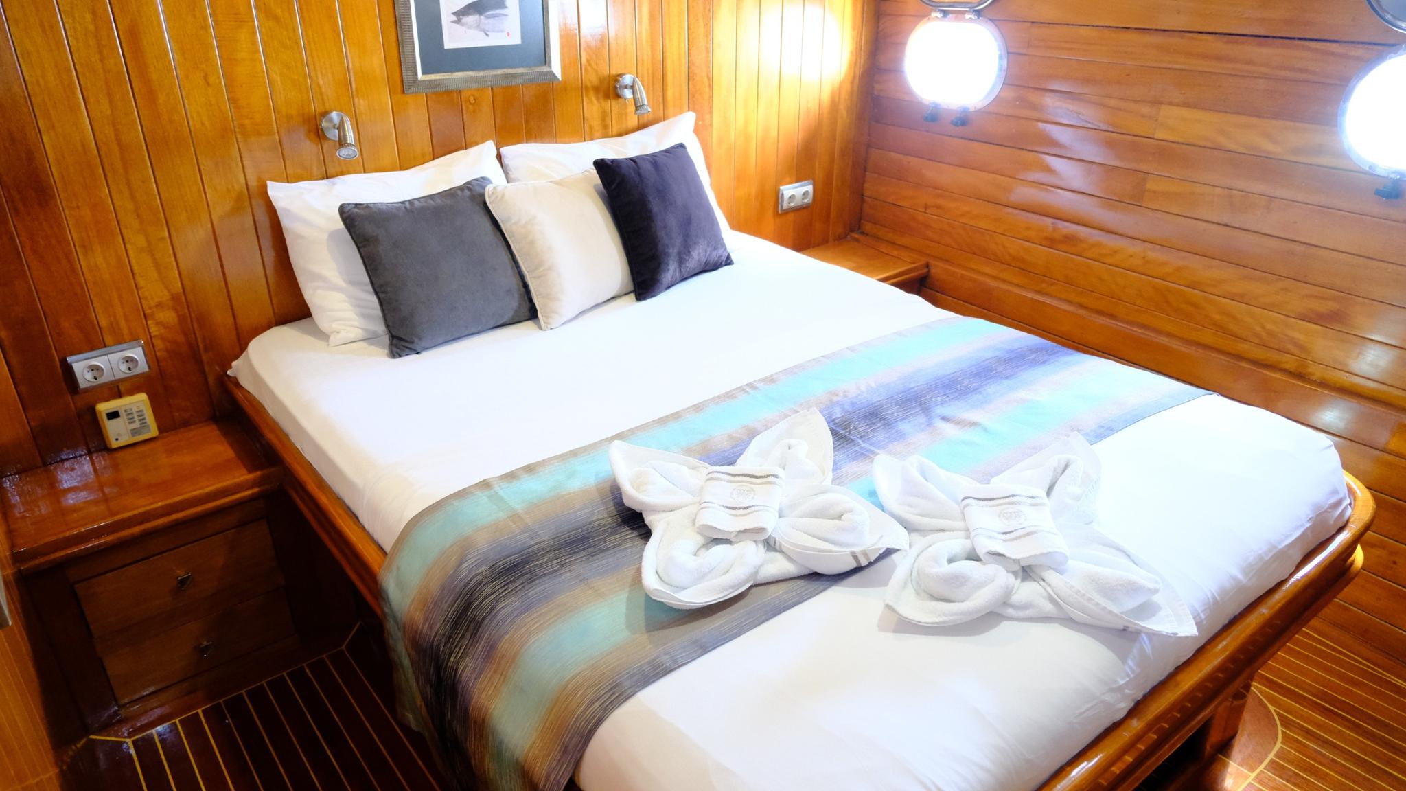 yacht guest cabin with double bed, gray pillows, and warm wood paneling