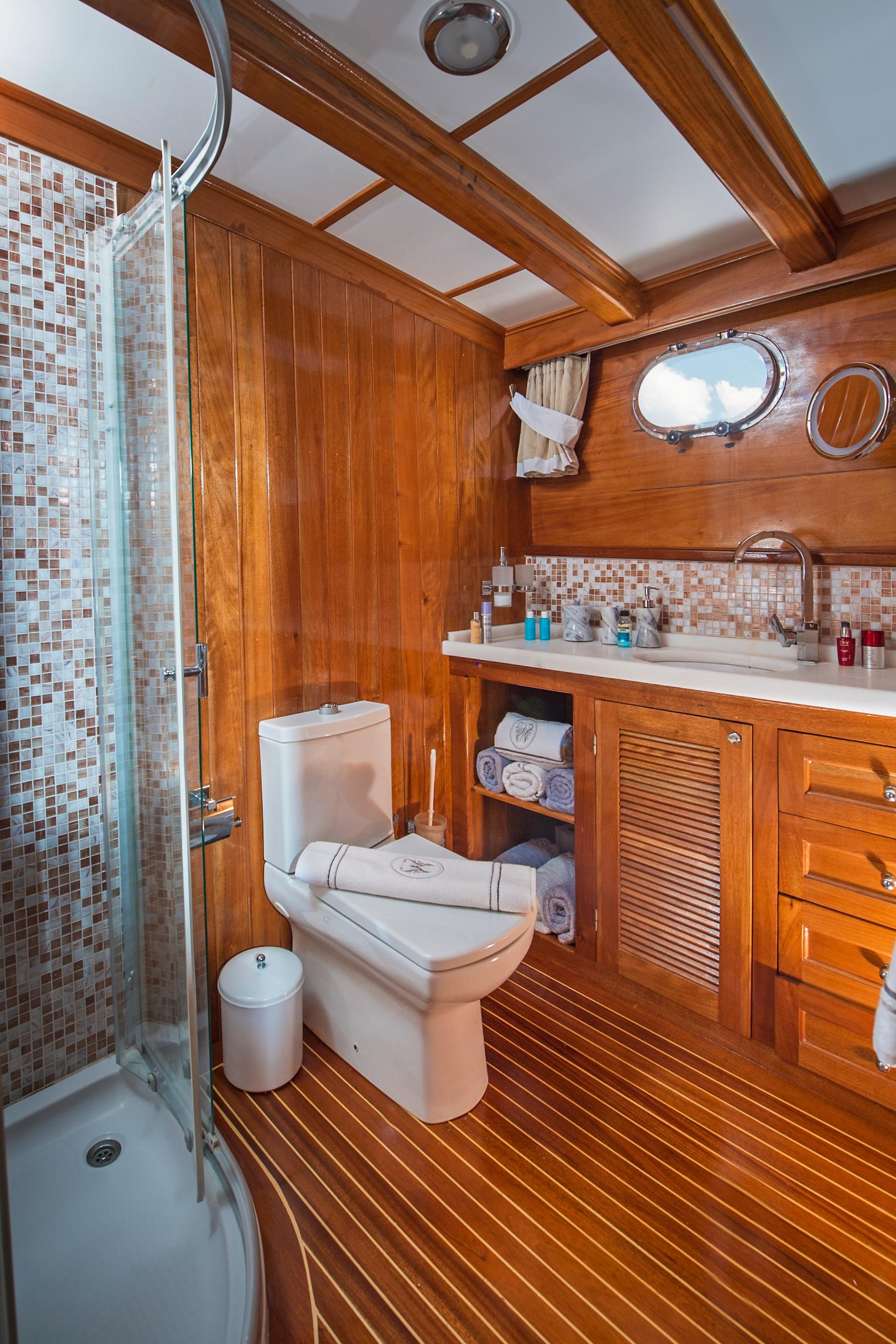 yacht ensuite bathroom featuring mosaic tile shower, teak flooring, vanity with storage and portholes