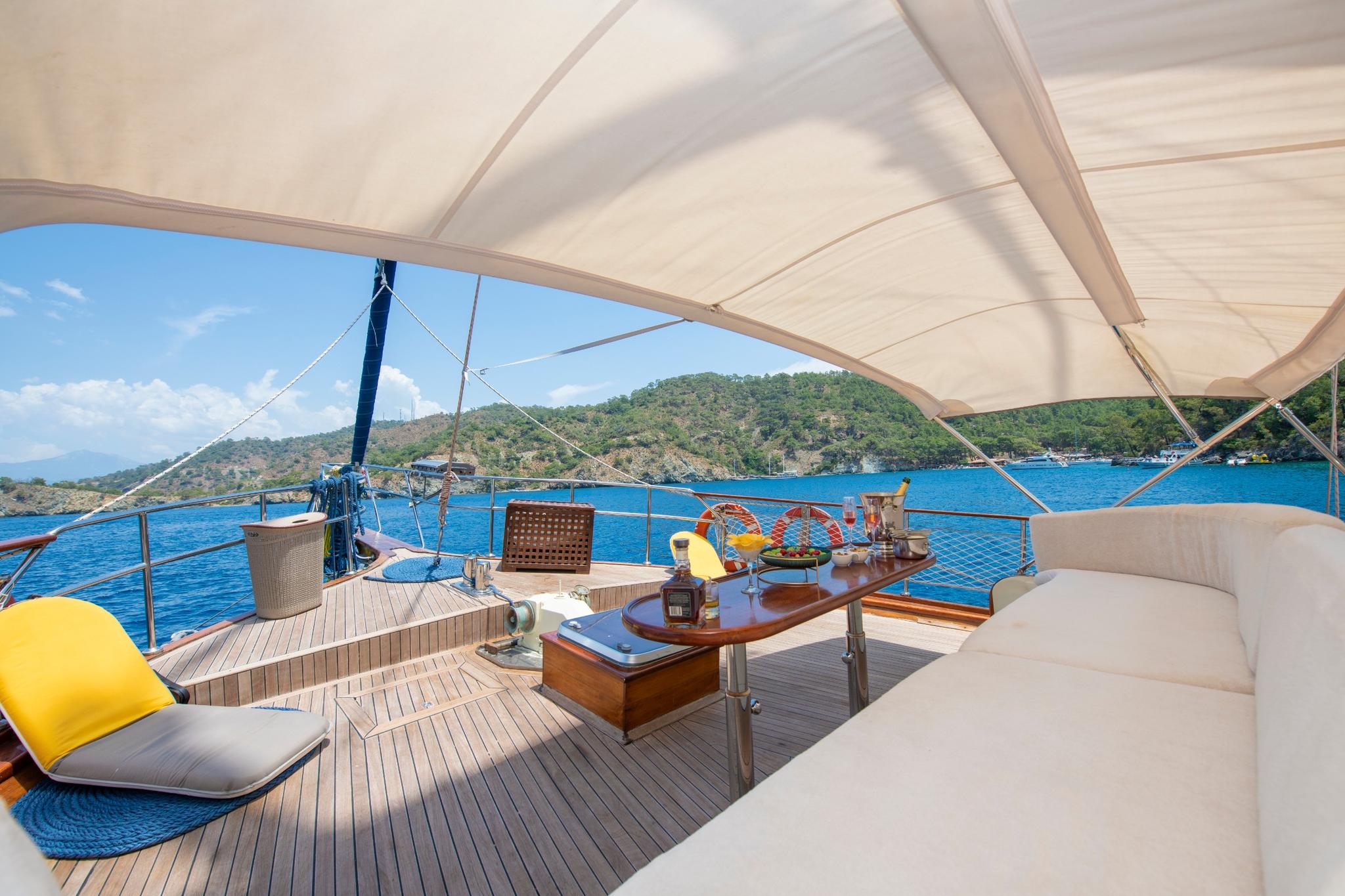 gulet bow deck with white cushioned seating, helm station, and canvas shade covering