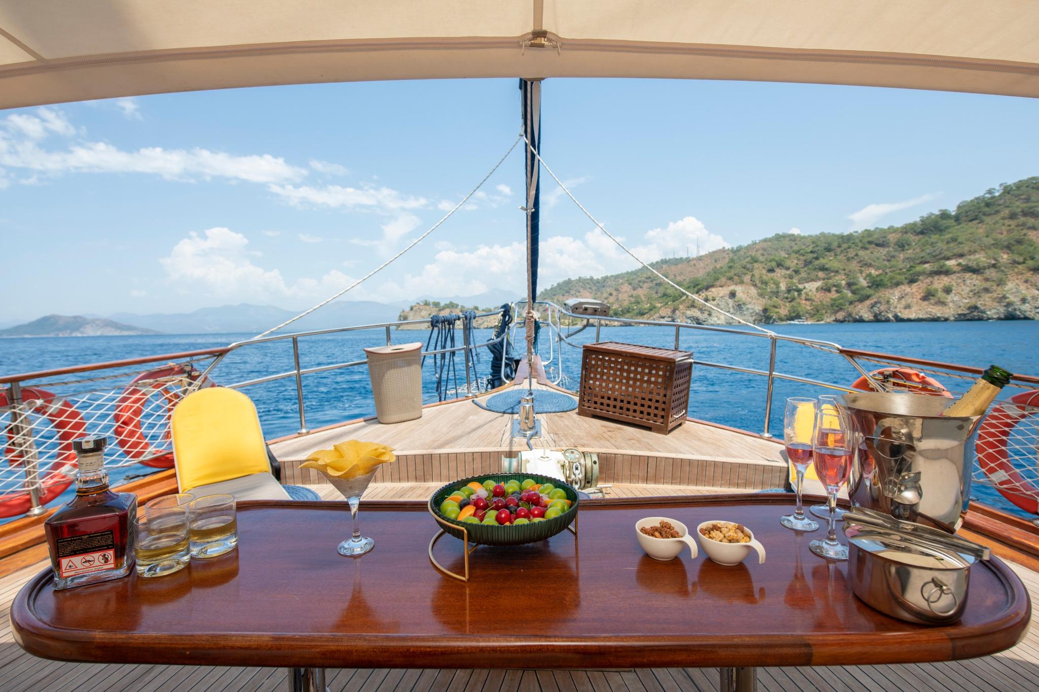 yacht dining table with fresh fruit bowl, champagne glasses, and snacks overlooking blue coastline