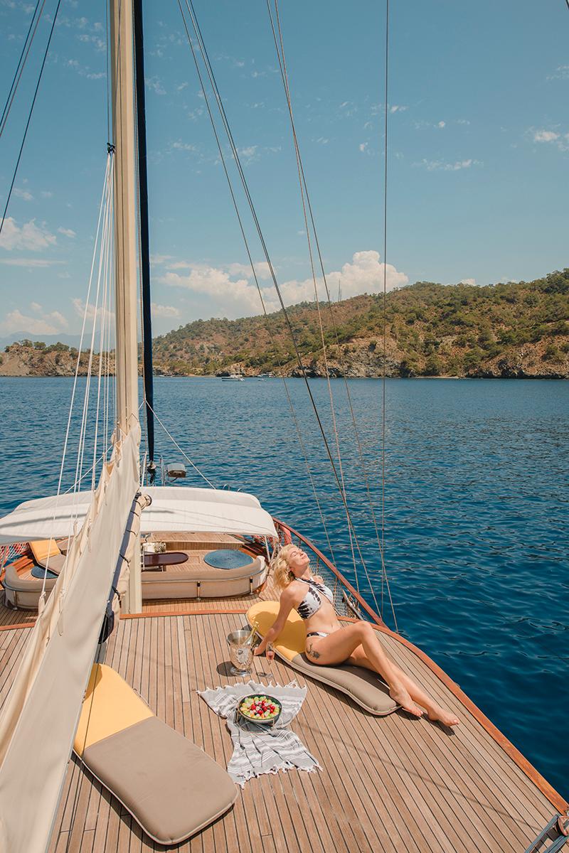 woman relaxing on teak foredeck with refreshments in Mediterranean bay
