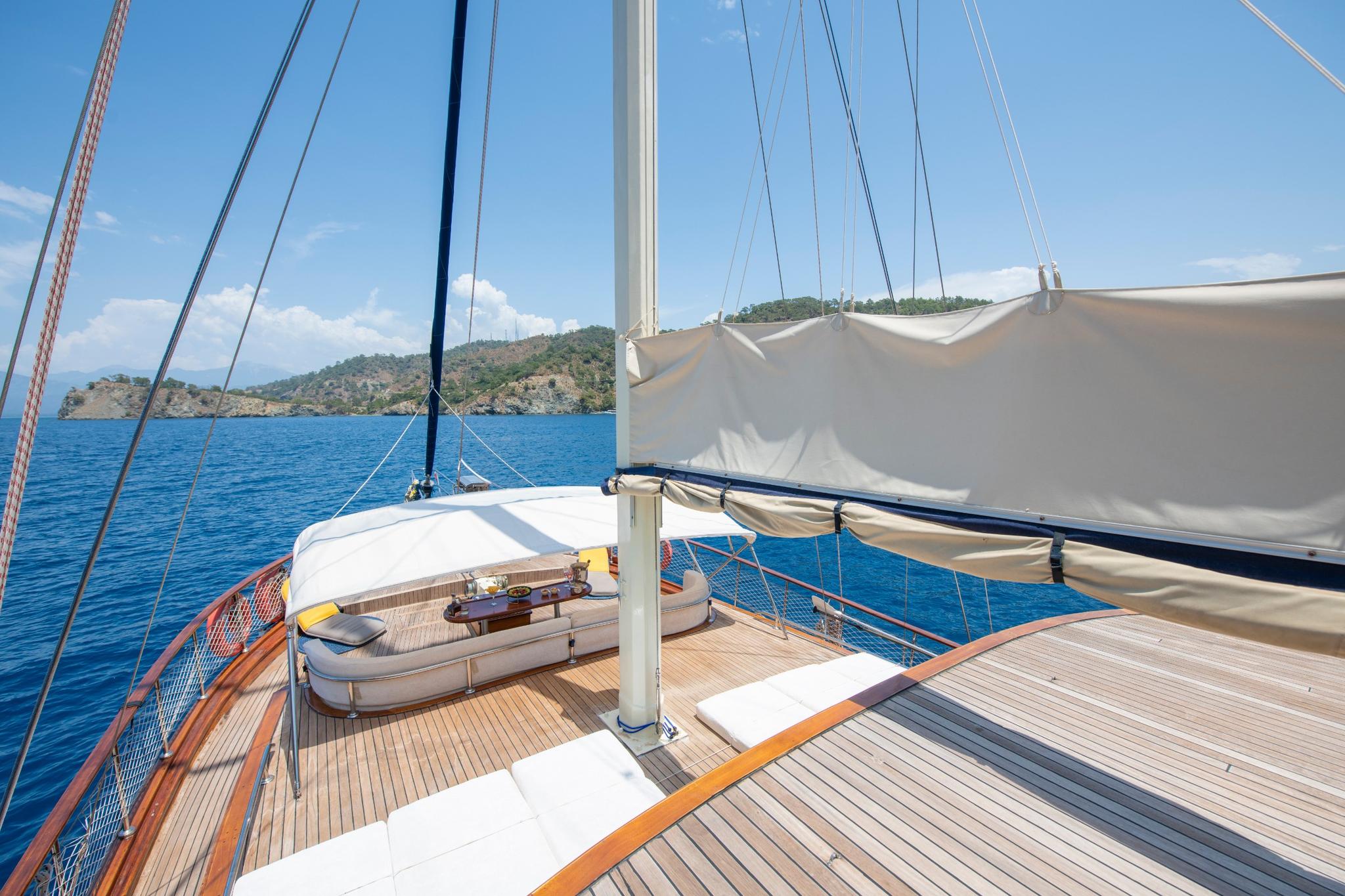 gulet forward deck with curved white seating area, mast, rigging and coastal views