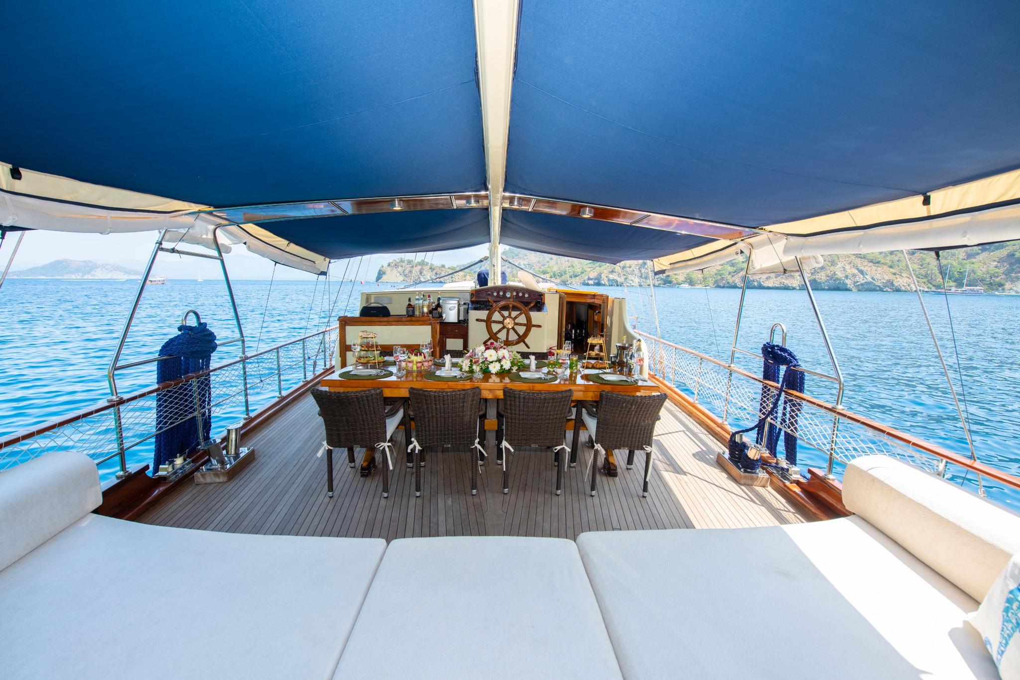 Gulet aft deck dining area with wooden table, wicker chairs under blue awning
