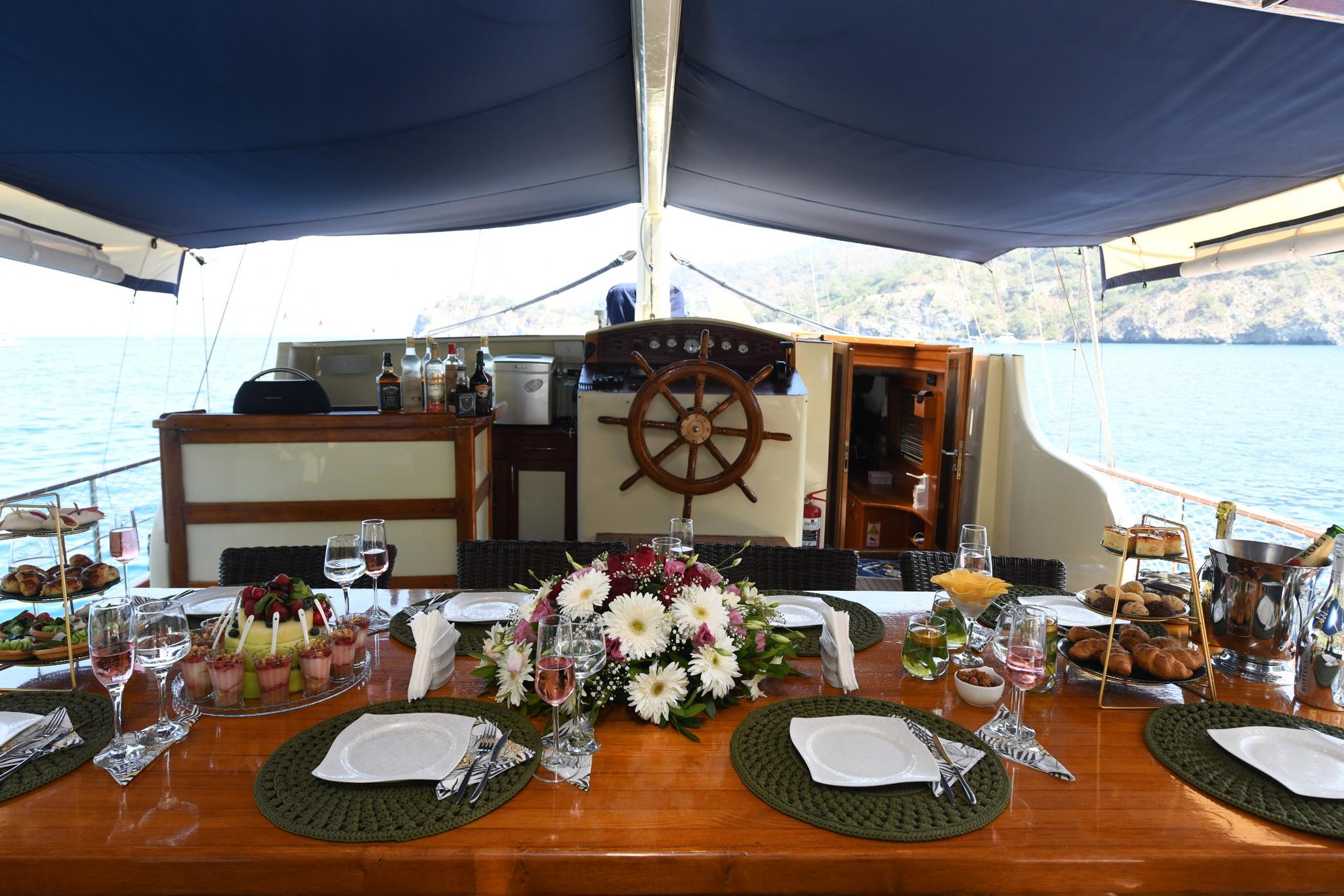 elegant yacht dining table set with plates, glasses, fresh flowers and food under blue awning