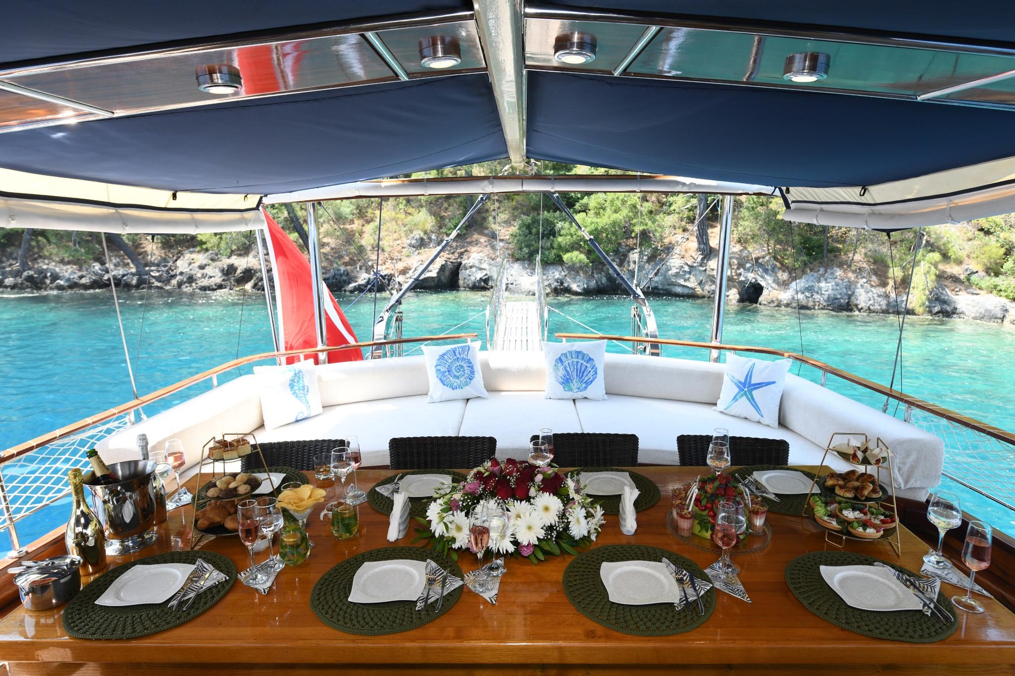 yacht aft deck dining table set with plates, wine glasses, food platters and floral centerpiece