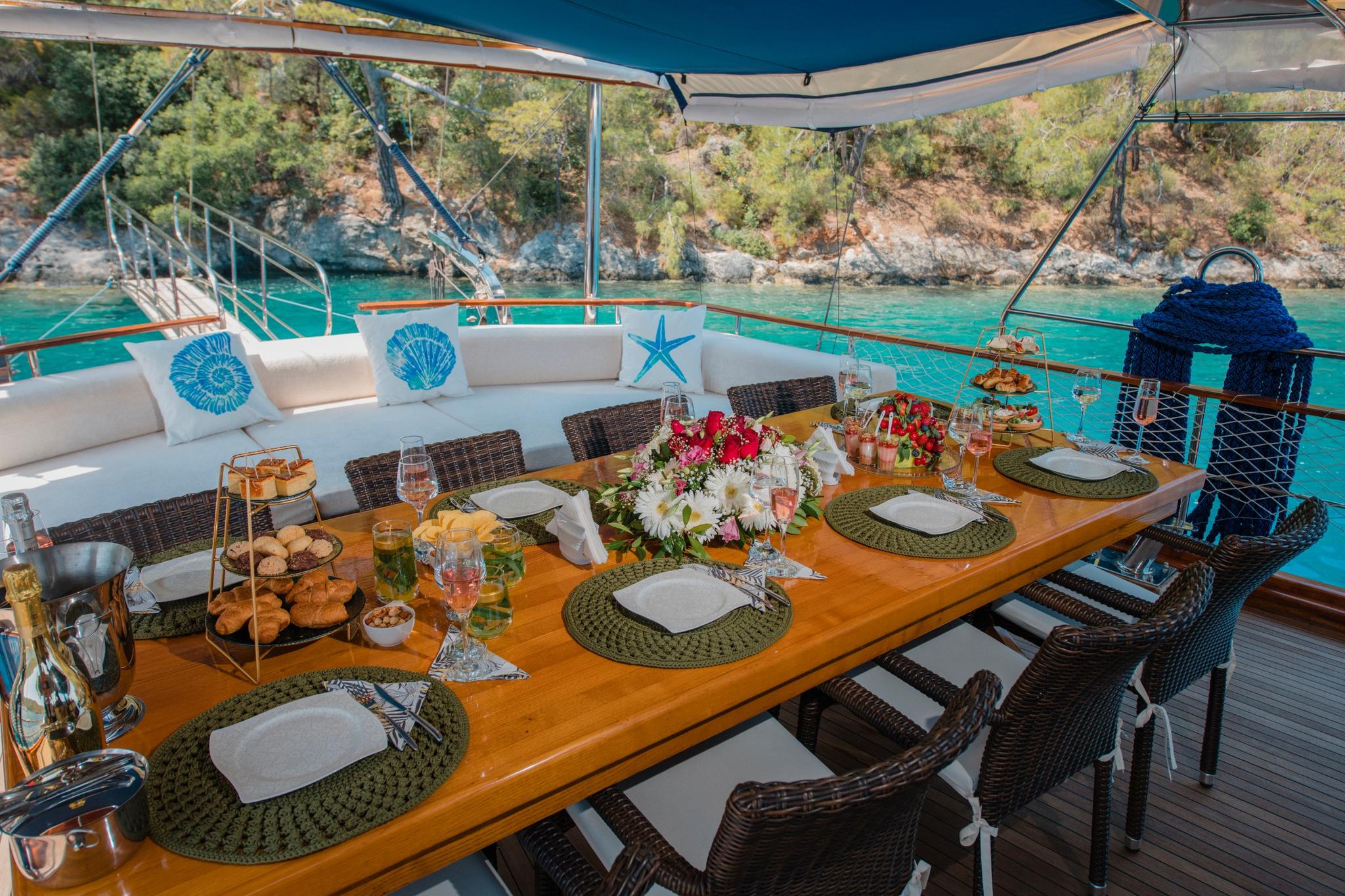 yacht aft deck dining table with served food, wine glasses, floral centerpiece and turquoise bay view