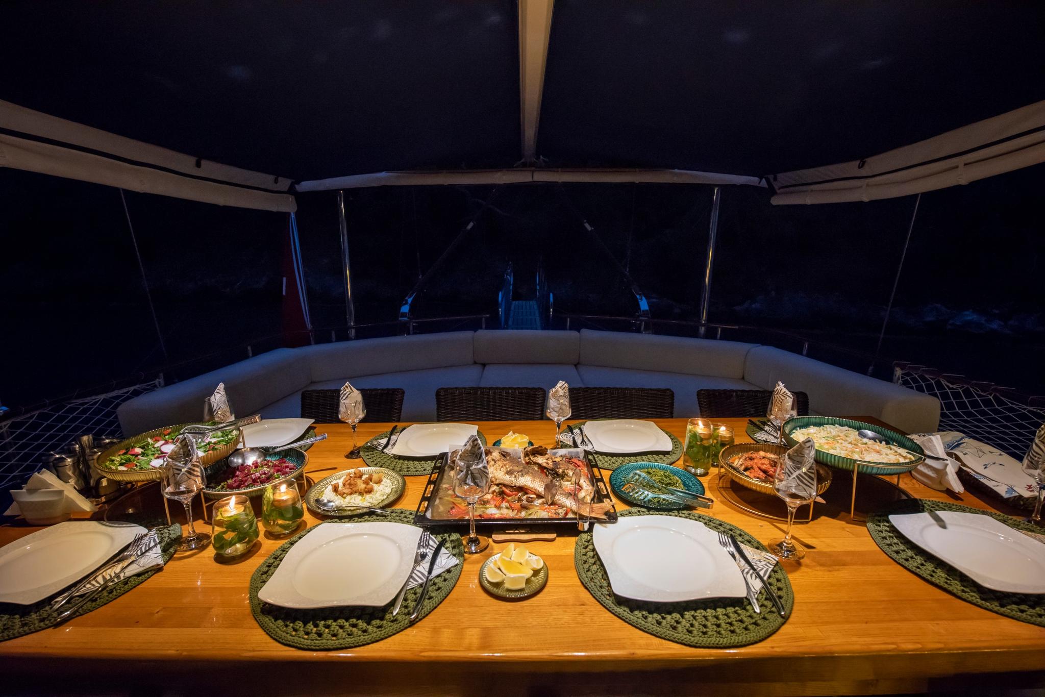 yacht dining table set for dinner with seafood dishes, plates, glasses and candles at night